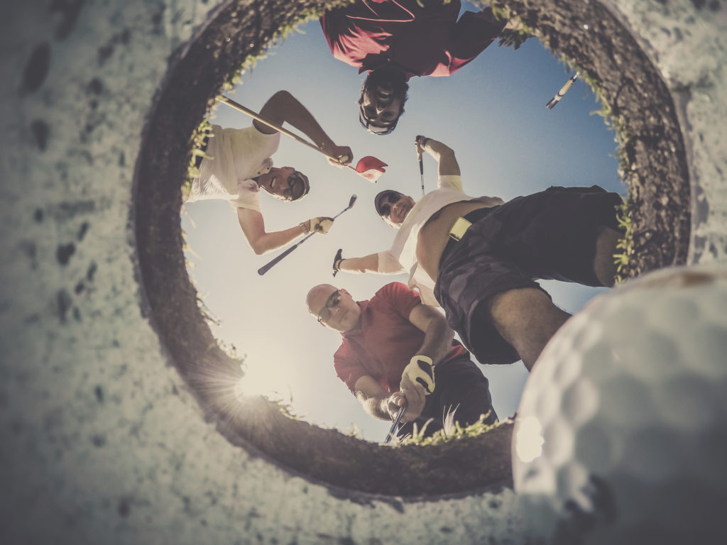 A Point Of View picture of 4 Golf Players and Golf Ball view From Inside the Hole on a sunny day of summer. The players are excited and happy.